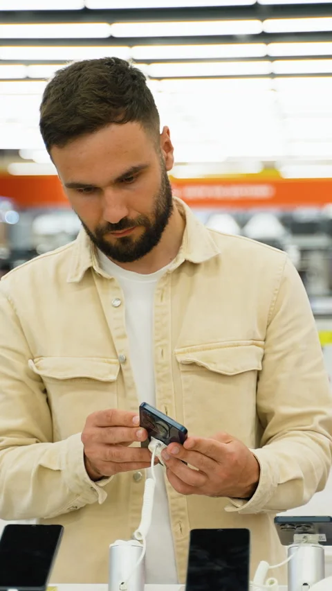 Customer evaluating smartphones in electronics store Stock Footage 317735556