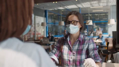 Customer in face mask and gloves giving order to waitress at counter in Stock Footage 134545288