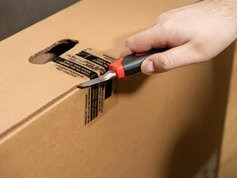 Customer hand opening a large brown cardboard shipping box with a utility k.. Stock Photos