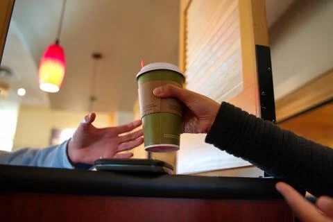 Customer hand passing over a hot beverage to a friend over restaurant partiti Stock Photos