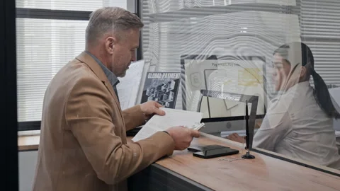 Customer Handing Card and Document to Bank Teller Through Slot in Bank Office Stock Footage 330963967