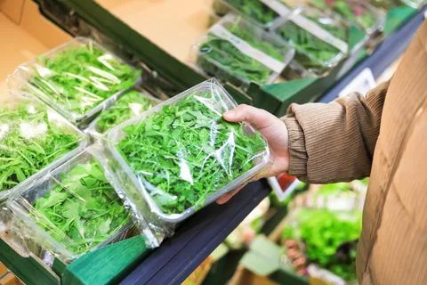 Customer holding a plastic container of fresh green arugula leaves while sh.. Stock Photos
