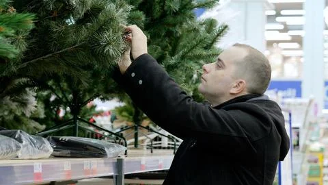 Customer inspecting artificial christmas tree in supermarket, checking quality Fotos de archivo