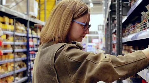 Customer making purchasing decisions, carefully examining goods on shelves in Stock Photos