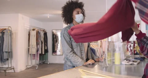 Customer paying for goods in clothes store wearing protective face mask during Stock Footage 136416784