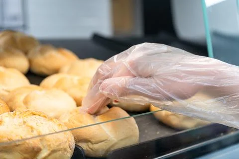 Customer selecting fresh bread roll with disposable glove at self service b.. Stock-Fotos