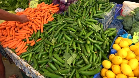 Customer selecting fresh carrots and cucumbers at local market Stockbeeldmateriaal 344972401