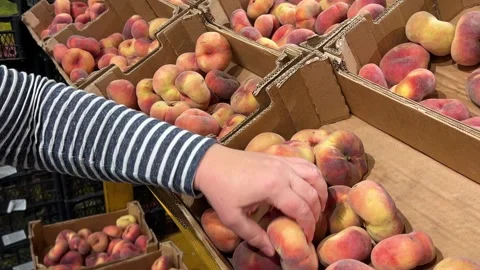A customer selects and picks up peaches from cardboard boxes at a supermarket. Stock Footage 318612213