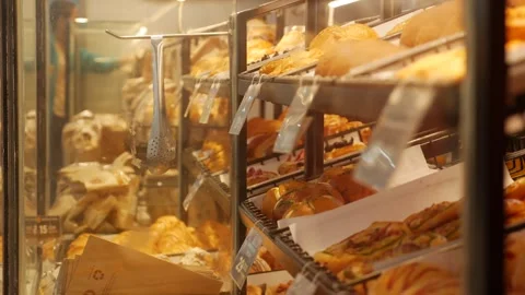A customer selects fresh baked goods from a glass bakery display in a Stock Footage 331943894