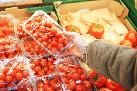 A customer selects a plastic container of bright red cherry tomatoes from a.. Stock Photos