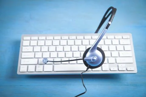 Customer service headset and computer keyboard on the blue background. Stock Photos