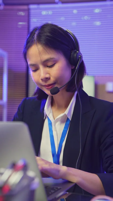 Customer service representative wearing microphone headset and working on laptop 動画素材 335804801