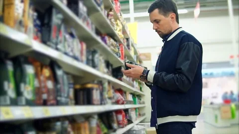 Customer in the supermarket. Man reading the label on the pack of the coffee Stock Footage 76769953