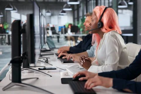 Customer Support Agent Assists Client Using Computer Headset In Busy Office. 库存照片