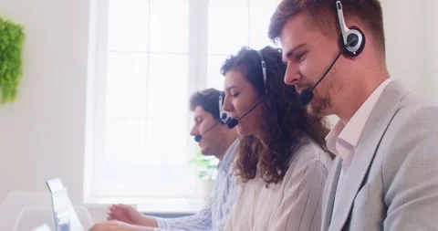 Customer support agents in headsets talking to clients and providing remote Stock Footage 330716276