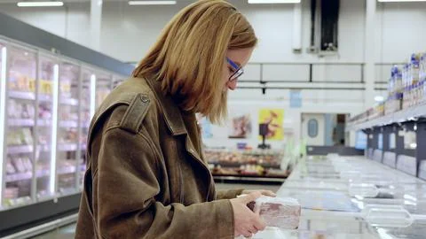 Customer thoughtfully inspecting packaged meat in grocery store refrigerated Stock Photos