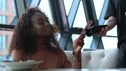 A customer uses her smartphone to make an electronic payment and pay her bill at Stock-Footage 267728321