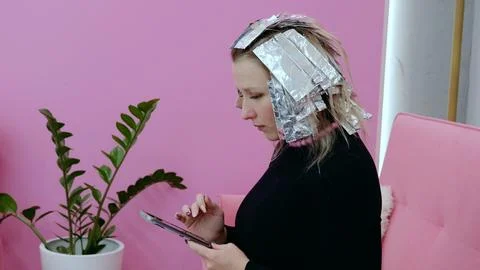 Customer uses her smartphone while waiting with foil in her hair during a Stock Photos