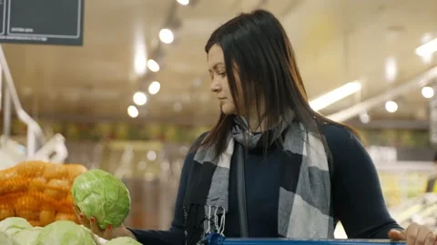 A customer in the vegetable section of a supermarket vibrates a head of cabbage Stock Footage 241790552