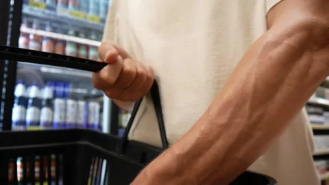A customer's hand putting a can of beer into a grocery basket in a supermarket Vídeos de archivo 339202937