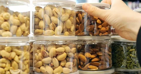 Customer's hand selecting a jar of almonds from a display of various nuts in Stock Footage 309047949