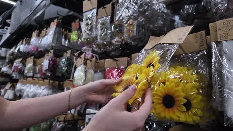 Customer's hand selects vibrant artificial sunflower heads in clear packagi.. Stock Footage 318831992