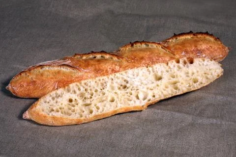 Cut across the long white bread lies on a grey linen tablecloth Stock Photos