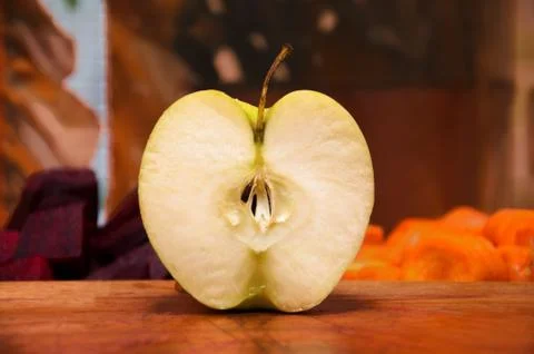 Cut an apple in half on a kitchen board against a background of sliced beets  Stock Photos