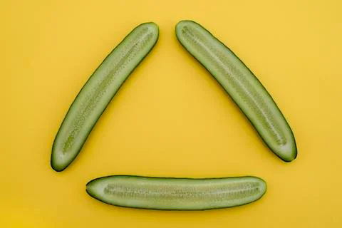 Cut cucumbers in half lengthwise in the shape of a triangle on a yellow backg Stock Photos