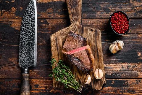 Cut fried rump cap or brazilian picanha beef meat steak on a wooden board. Dark Stock Photos
