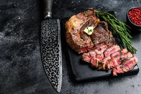 Cut Grilled Chuck eye roll beef meat steak on a marble board. Black background Stock Photos