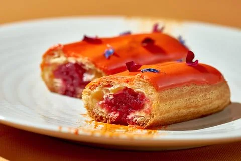 Cut in half eclair with berry filling and custard in a plate. Close-up, sha.. Stock Photos