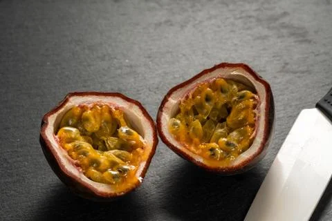 Cut in half fruit passion fruit on a black campa lies next to a ceramic knife Stock Photos