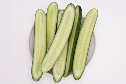 Cut in half lengthwise cucumbers on a plate on a white table Stock Photos