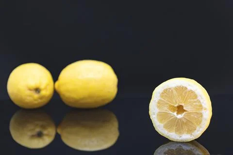 A cut lemon in the foreground and in focus with two more lemons in the Stock Photos