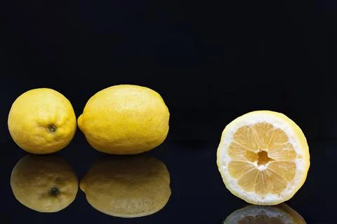 A cut lemon in the foreground with two more lemons on black background Foto stock