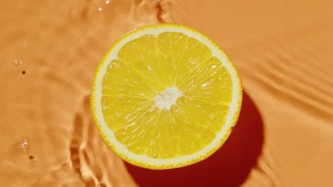 Cut lemon in water waves. Fresh aroma citrus on orange background top view Stock Footage 243668050
