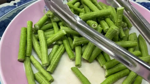 Cut long bean on pink plate with silver tongs close up shot Stock Footage 232086740