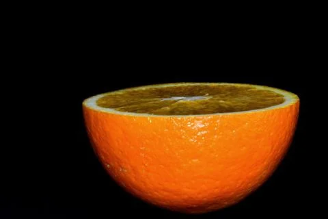 A cut orange on a black background. Stock Photos