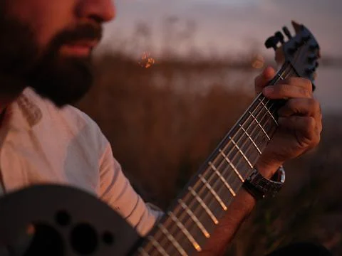 Cut-out focus on a person playing chords on a guitar by a lake at sunset Stock Photos
