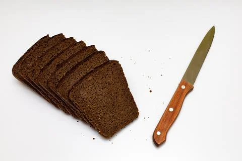 A cut piece of black bread next to which lies a knife Stock Photos