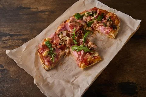 Cut into pieces rectangular Roman pizza with prosciutto ham, tomatoes Stock Photos