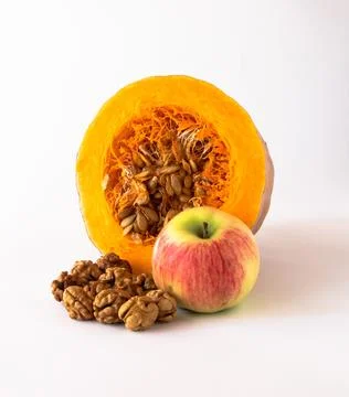 Cut pumpkin with seeds inside, apple, walnut kernels on a white background. Stock Photos