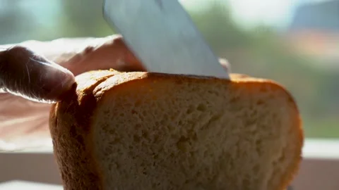 Cut a slice of bread. Fresh bread on a table near the window close-up, lit by Video stock 134609910