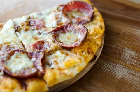 Cut into slice serving pizza with pepperoni sausage on a wooden board. Stock Photos