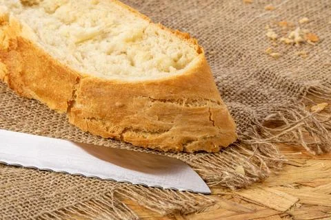 A cut slice of white wheat bread and a bread knife on a burlap napkin on a .. Stock Photos