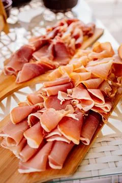 Cut into thin pieces of jamon on cutting board for a banquet. Stock Photos