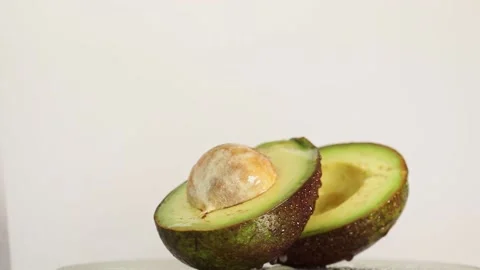 Cut into two pieces of avocado with drops of water rotates on the table Stock Footage 152761292
