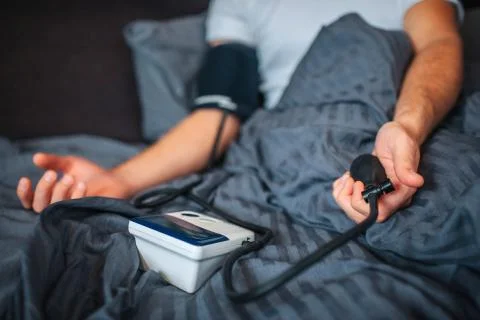 Cut view of man lying on bad with covered low part of body. He uses device fo Stock Photos