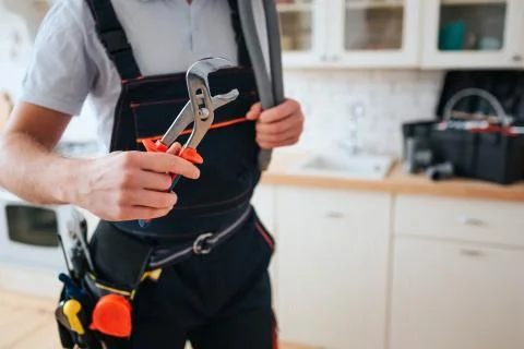 Cut view of man in working uniform hold wrench. He stand in kitchen. Daylight Stock Photos
